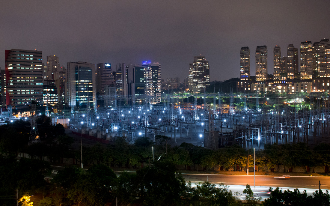 Hay una subestación de ISA. Es de noche y al fondo hay una ciudad iluminada.