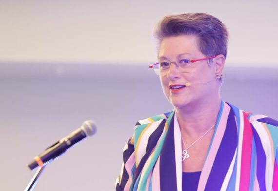 foto de fabienne. Está en un auditorio. Luce camisa a rayas de colores. Está hablando sobre sociología del futuro